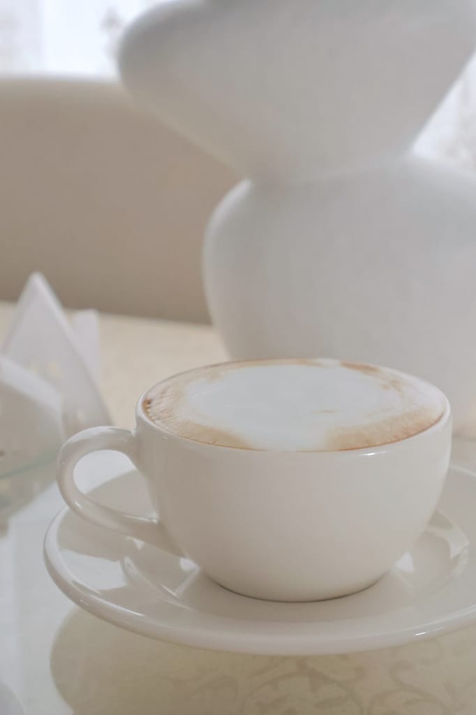 A clean, minimalist shot of a white coffee cup with foam art on a table.