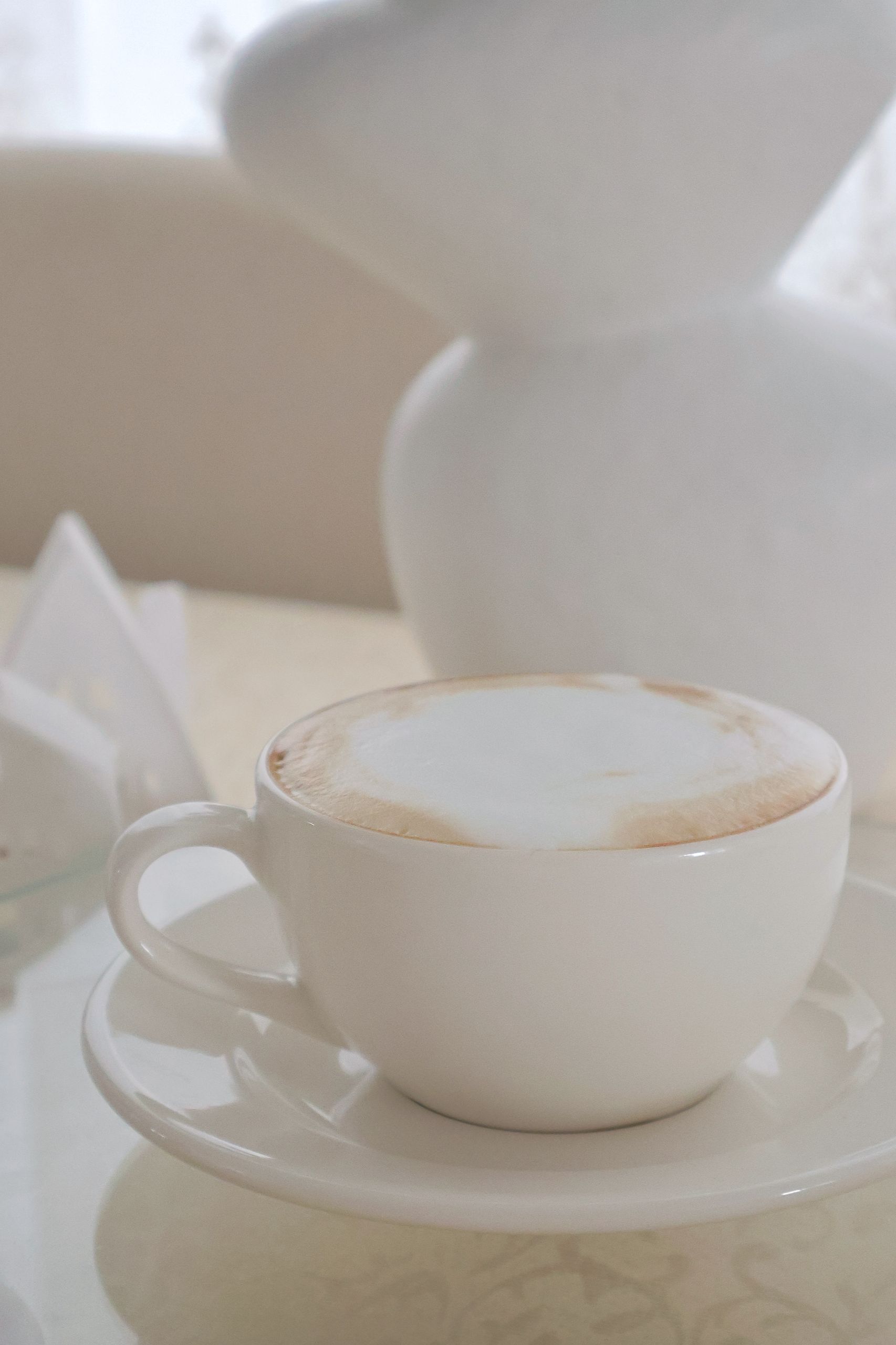 A clean, minimalist shot of a white coffee cup with foam art on a table.